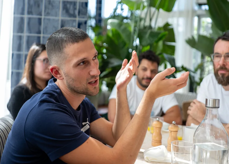 Someone mid-explanation, hands up, with the table listening